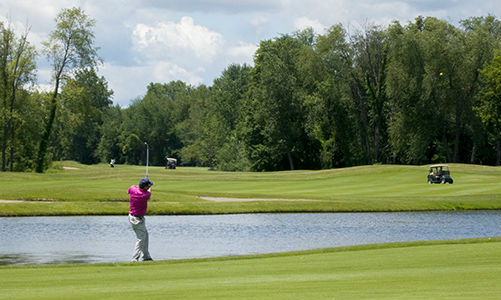 Golfer taking shot over a water hazard onto green 