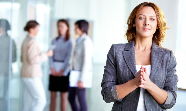 woman in grey blazer with hands together looking at camera